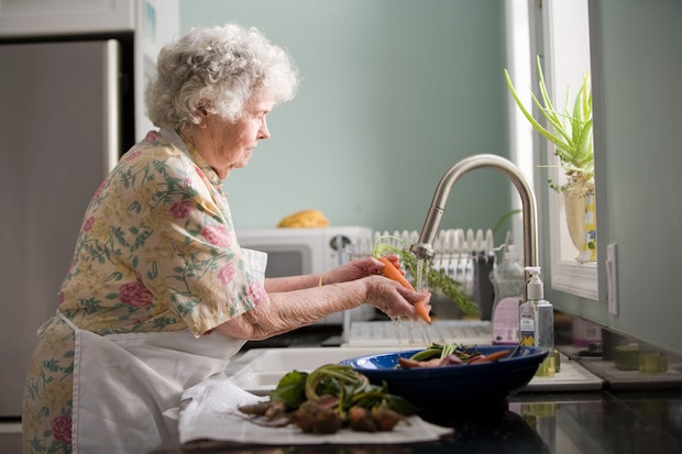 an old woman washing vegetables at the sink