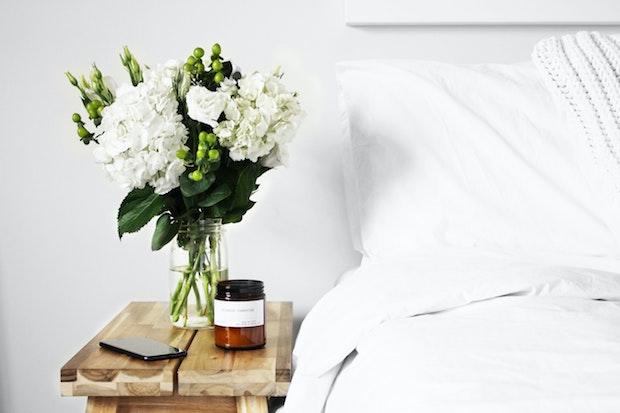 a white bed next to a wood bedside table