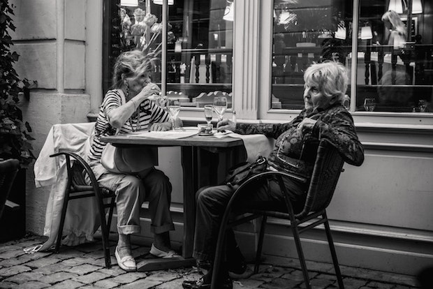 two older women sitting at a table drinking out of wine glasses