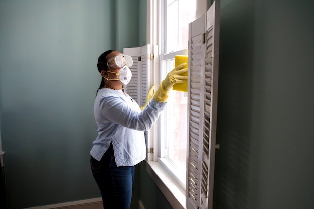 a woman wearing gloves and a mask and cleaning windows