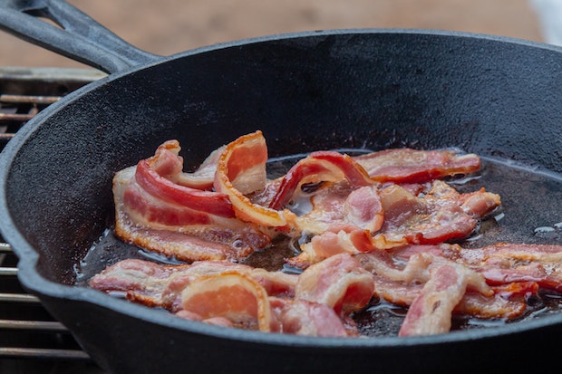 bacon strips frying in a cast iron pan